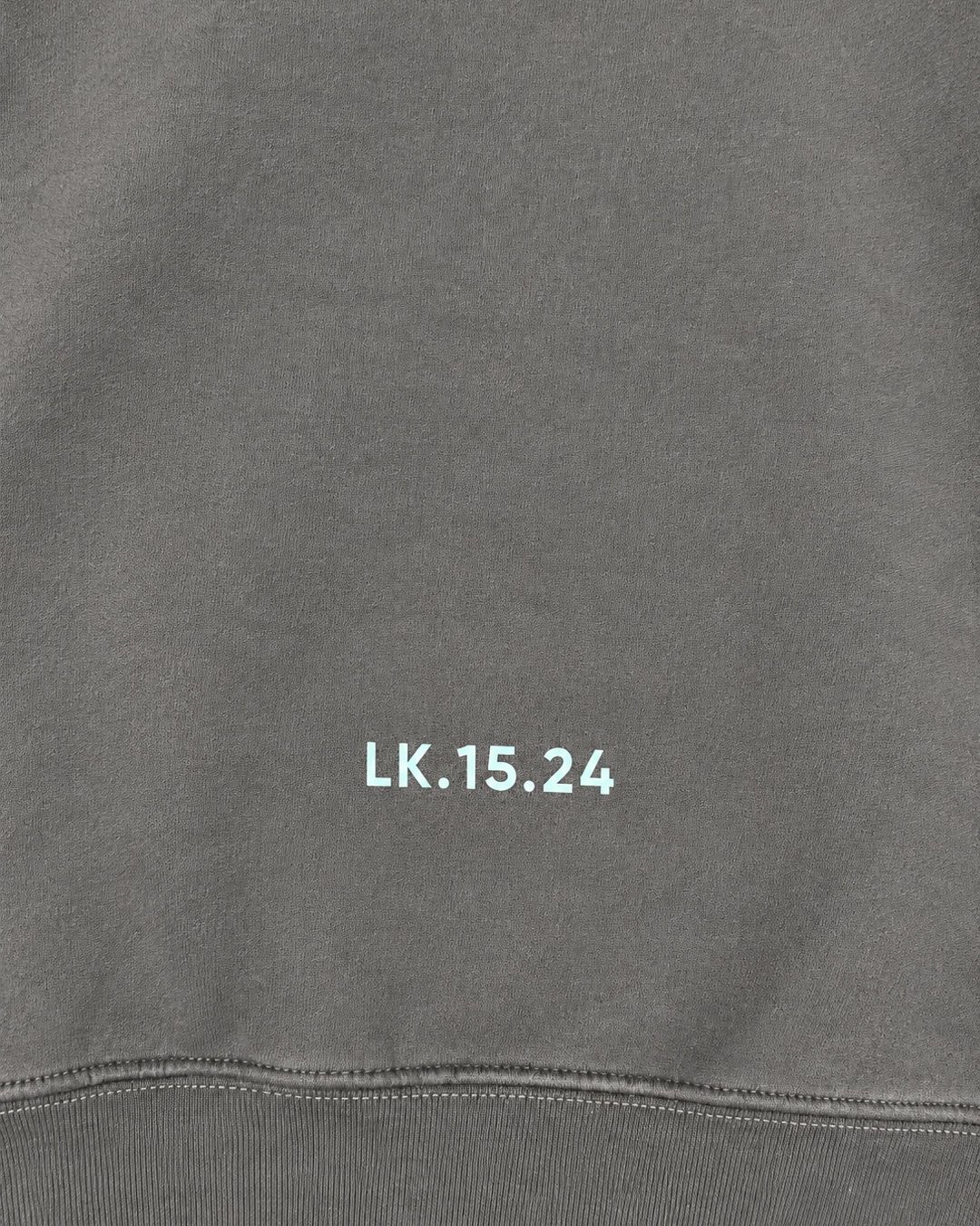 Close-up of the LK.15.24 print above the ribbed hem on the Ash hoodie