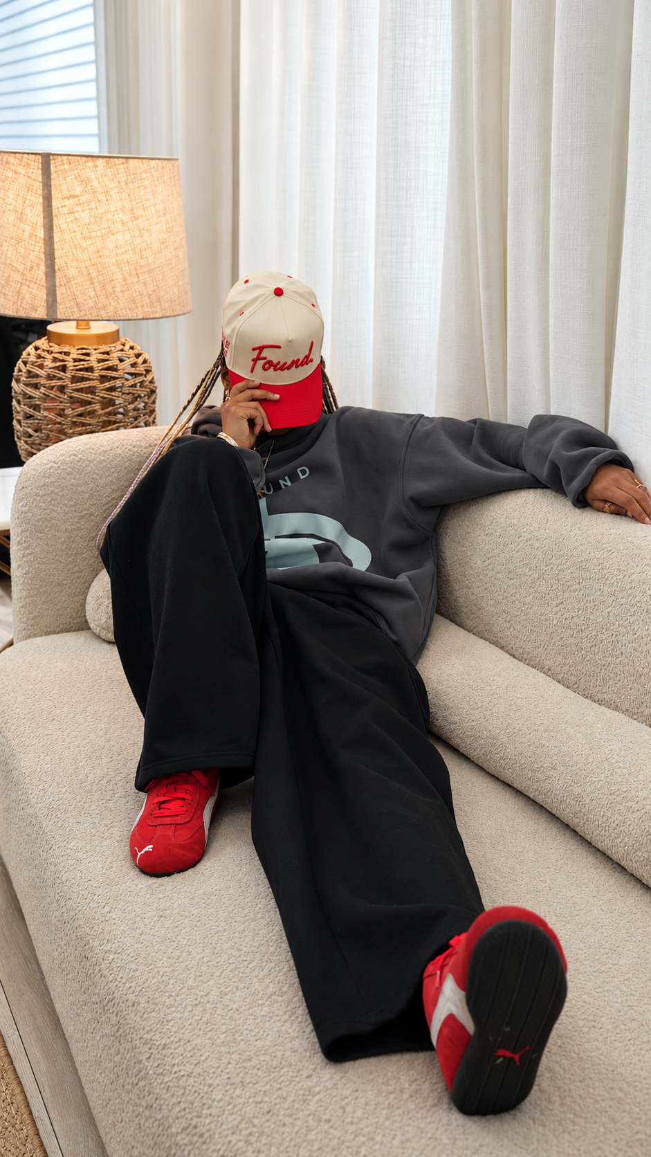 Model lounging on a couch wearing the Found Cap in red