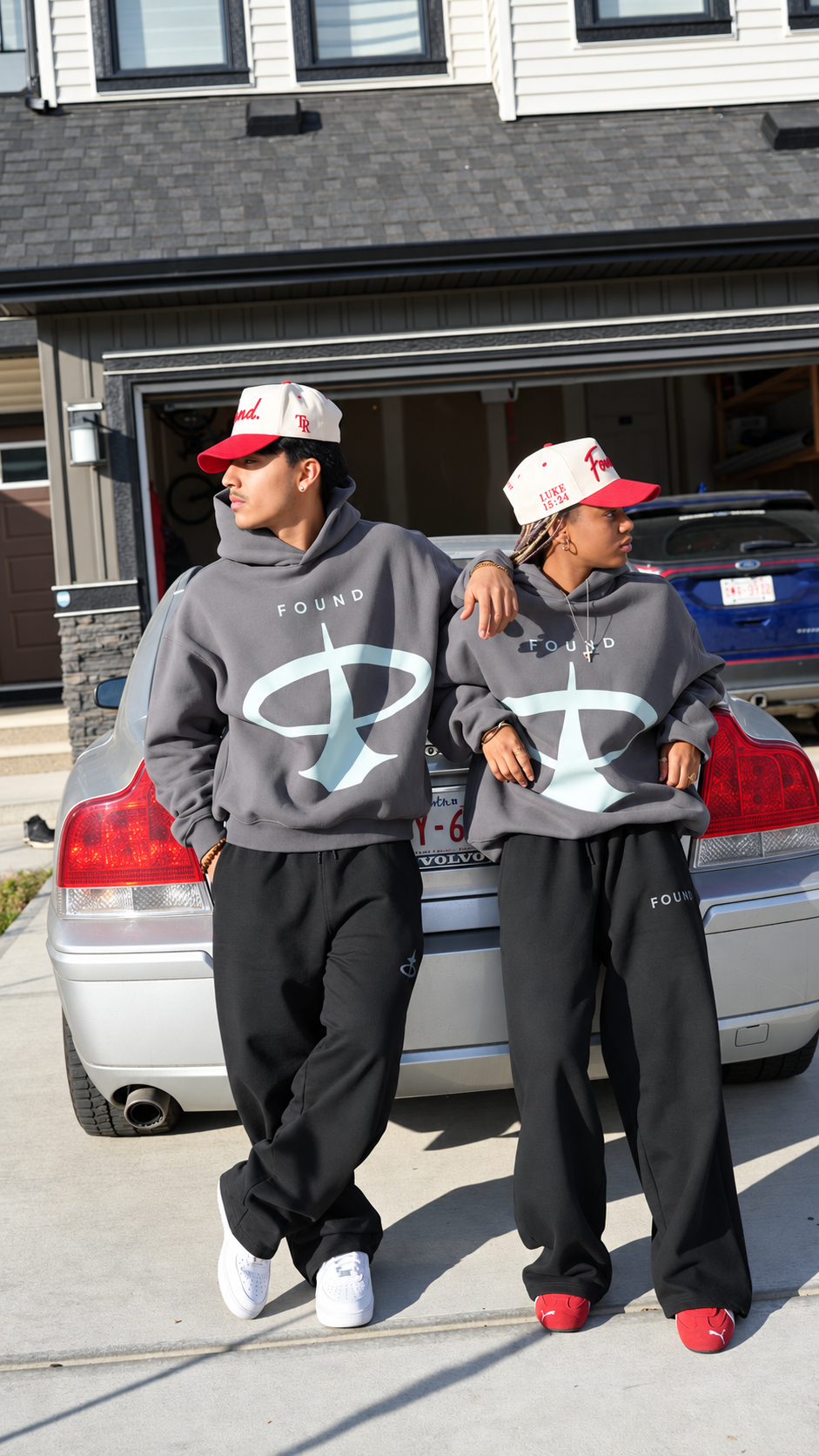 Two models in the FOUND Restoration Hoodie in Ash leaning on a car, FOUND wordmark and pale-aqua emblem on the chest
